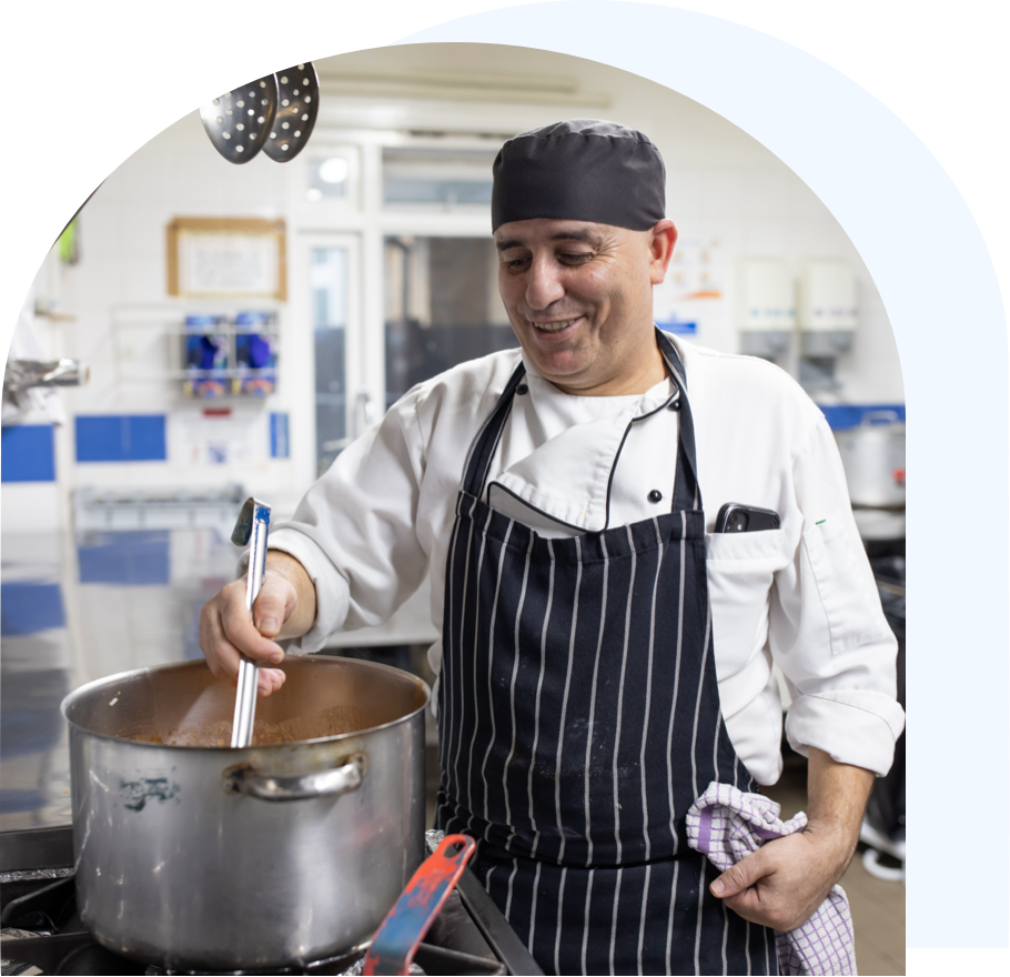 A chef stirring a metal pot of food on the hob